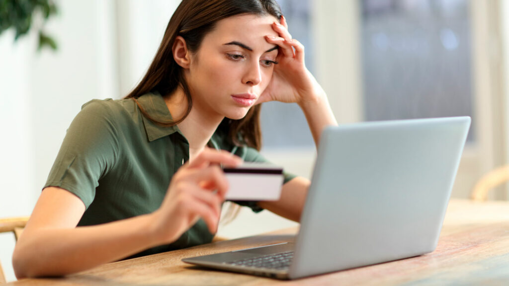 ung kvinne holder bankkort i hånden og ser oppgitt på pc-skjermen