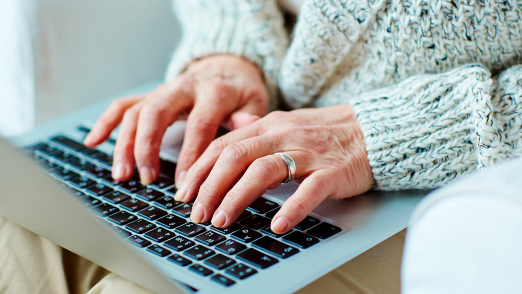 nærbilde av hender til eldre kvinne på tastatur. Det er viktig å ta grep for å øke sikkerhet når man bruker pc eller mac. 