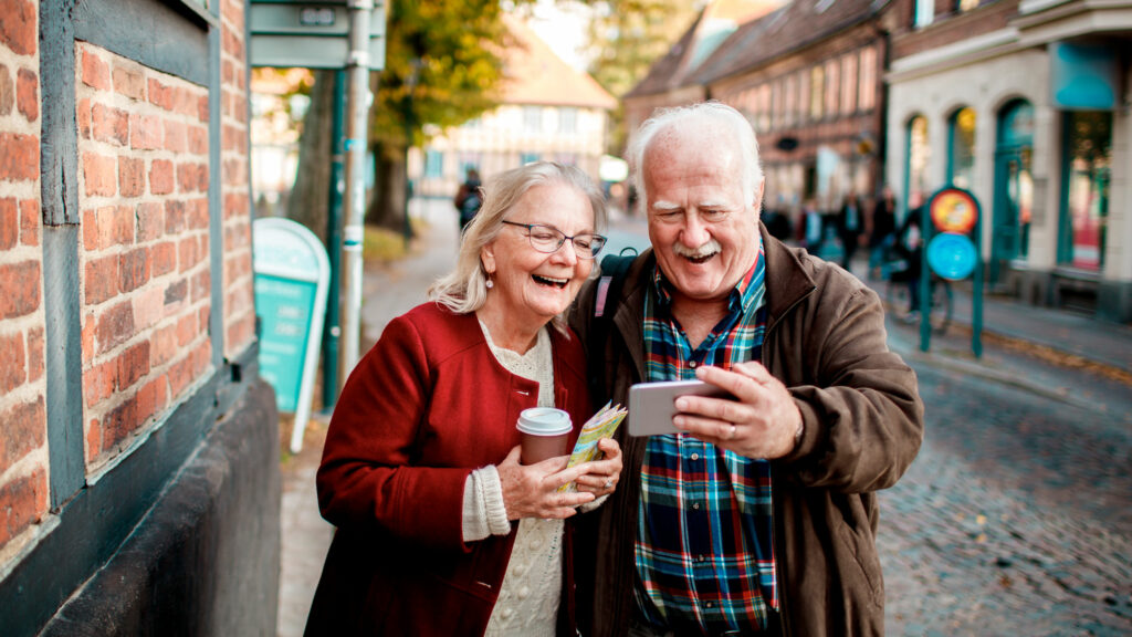 et eldre par, mann og dame, tar selfie med mobilen i gaten på en by