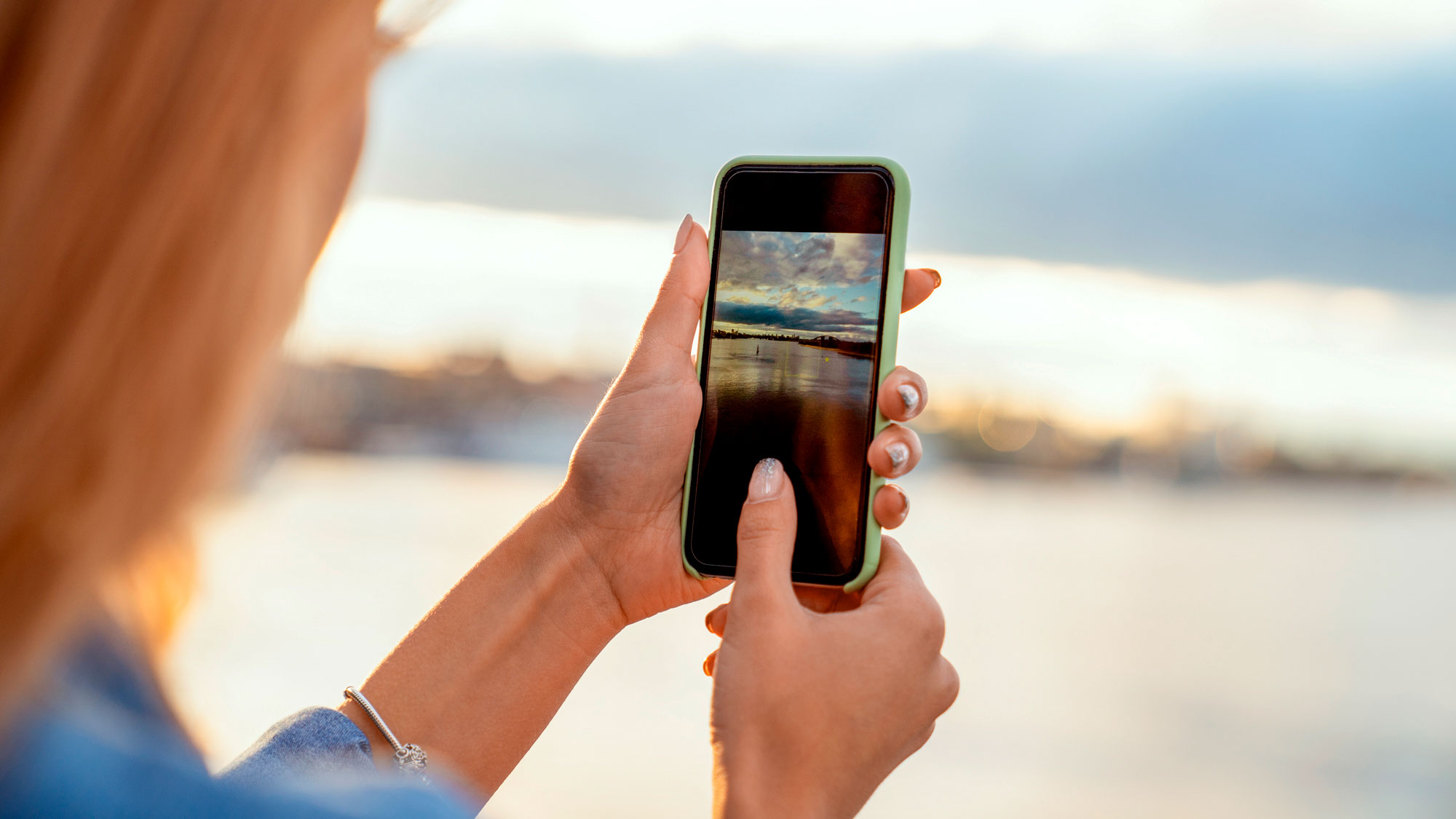 Kvinne bruker mobilen til å ta bilde av utsikten av hav og solnedgang