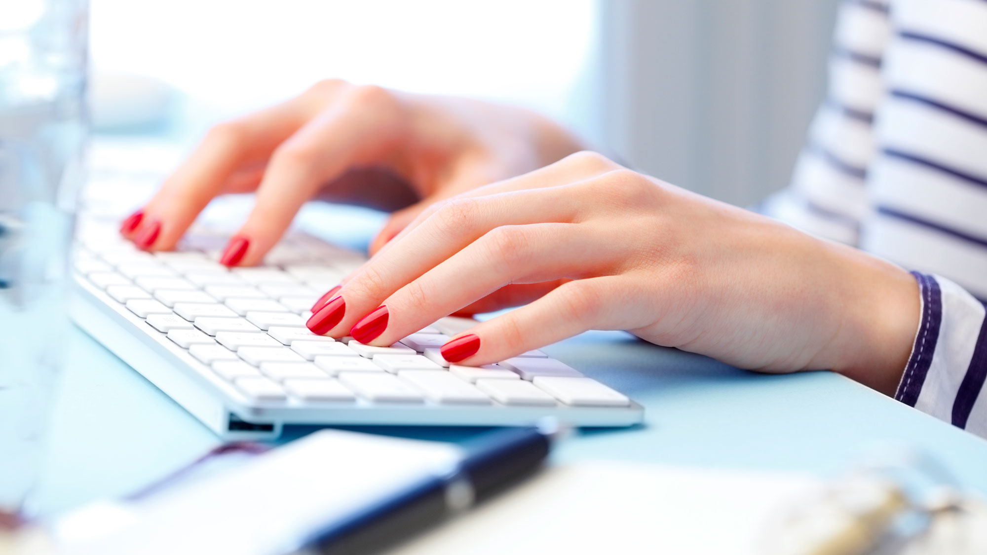 nærbilde av hender til ung kvinne med rød neglelakk på tastatur