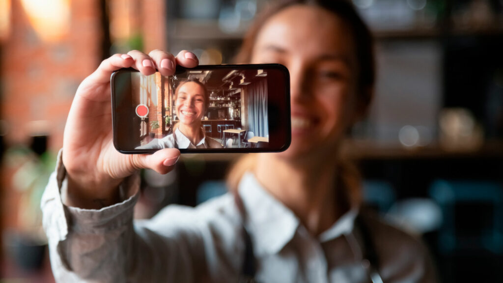 Ung kvinne tar en selfie / et bilde eller en video av seg selv med mobilen