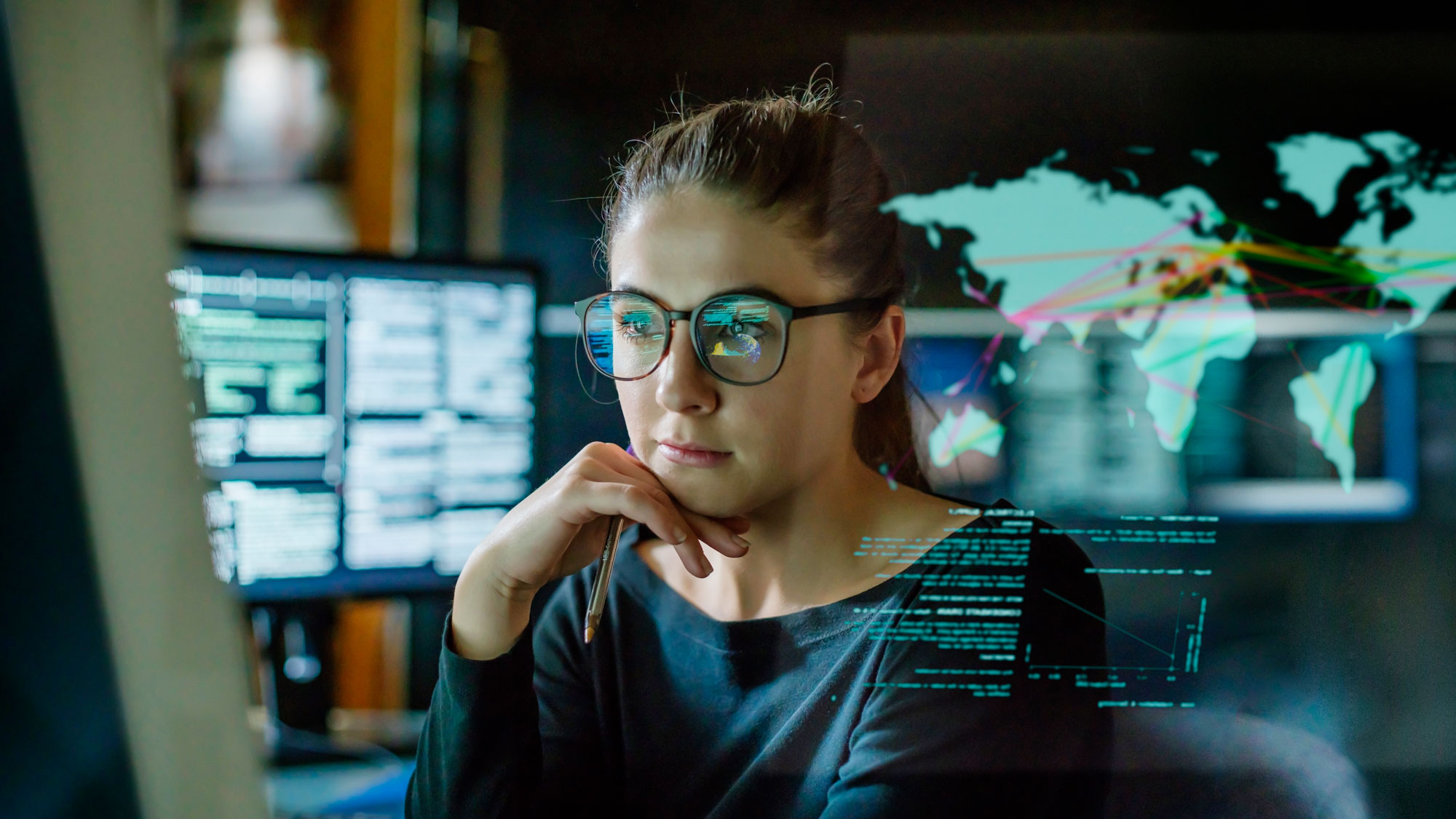 ung kvinne med briller med flere skjermer med koder og kart rundt seg