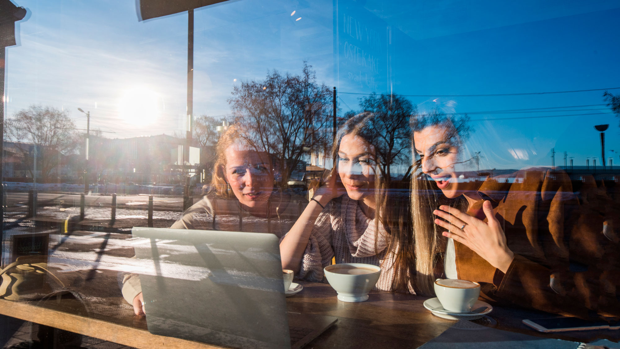 Tre damer i vindu på et kafe, mens de ser på en dataskjerm