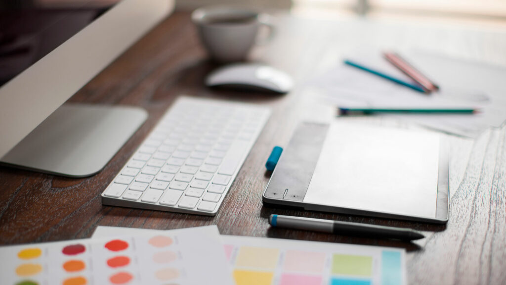 skrivebord med mac, blyanter og fargeprøver. kreativt rot