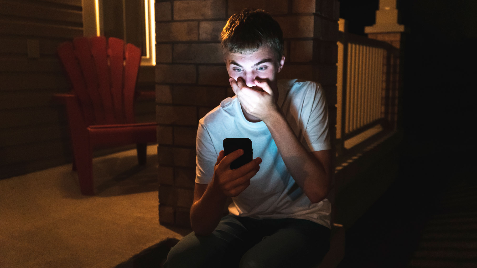 Ung tennåringsgutt ser skrekkslagen på mobilen mens han holder seg foran munn